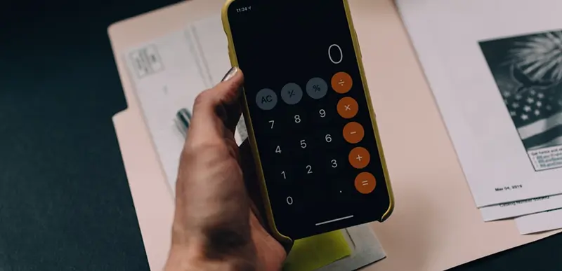 Ranka laiko telefoną su atvertu skaičiuotuvu virš dokumentų