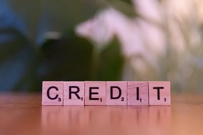 Mediniai Scrabble žaidimo kauliukai su užrašu CREDIT ant medinio stalo